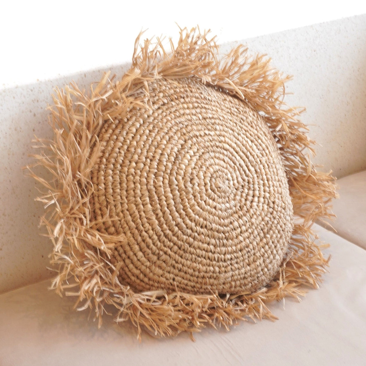 Soeji TARAKAN: rundes Raffia-Kissen mit Fransen auf heller Sitzfläche, schräge Nahansicht