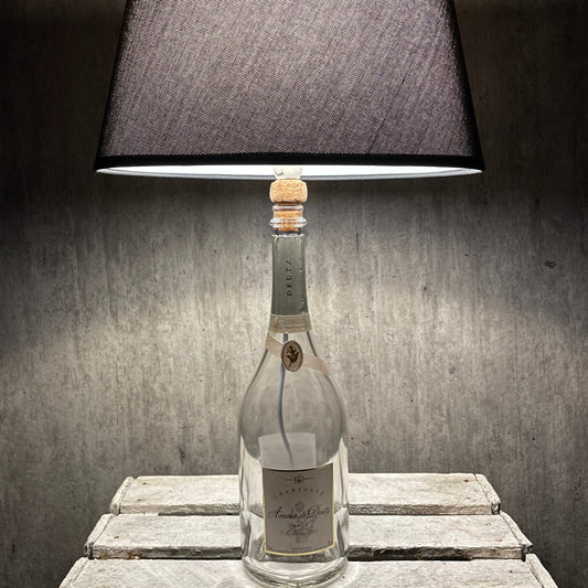 Amour de Deutz Champagnerflasche als Tischlampe mit dunklem Stoffschirm vor grauem Hintergrund